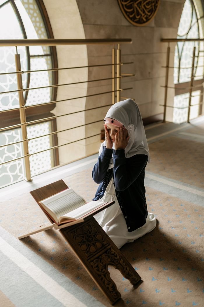 Daily Duas & Islamic Prayers Course A young girl kneels and prays in a mosque, reading the Quran. Islamic culture and tradition.
