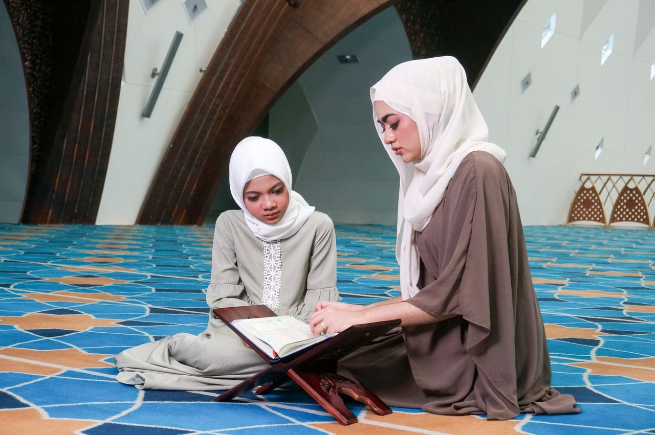 Two women wearing hijabs reading the Quran together inside a contemporary mosque with stylish design.